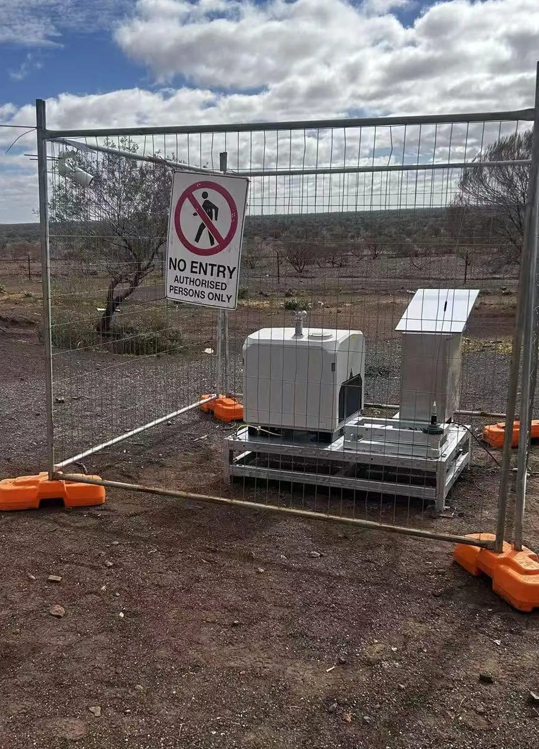 A drone dock and its equipment cabinet behind a fence with a no-entry sign