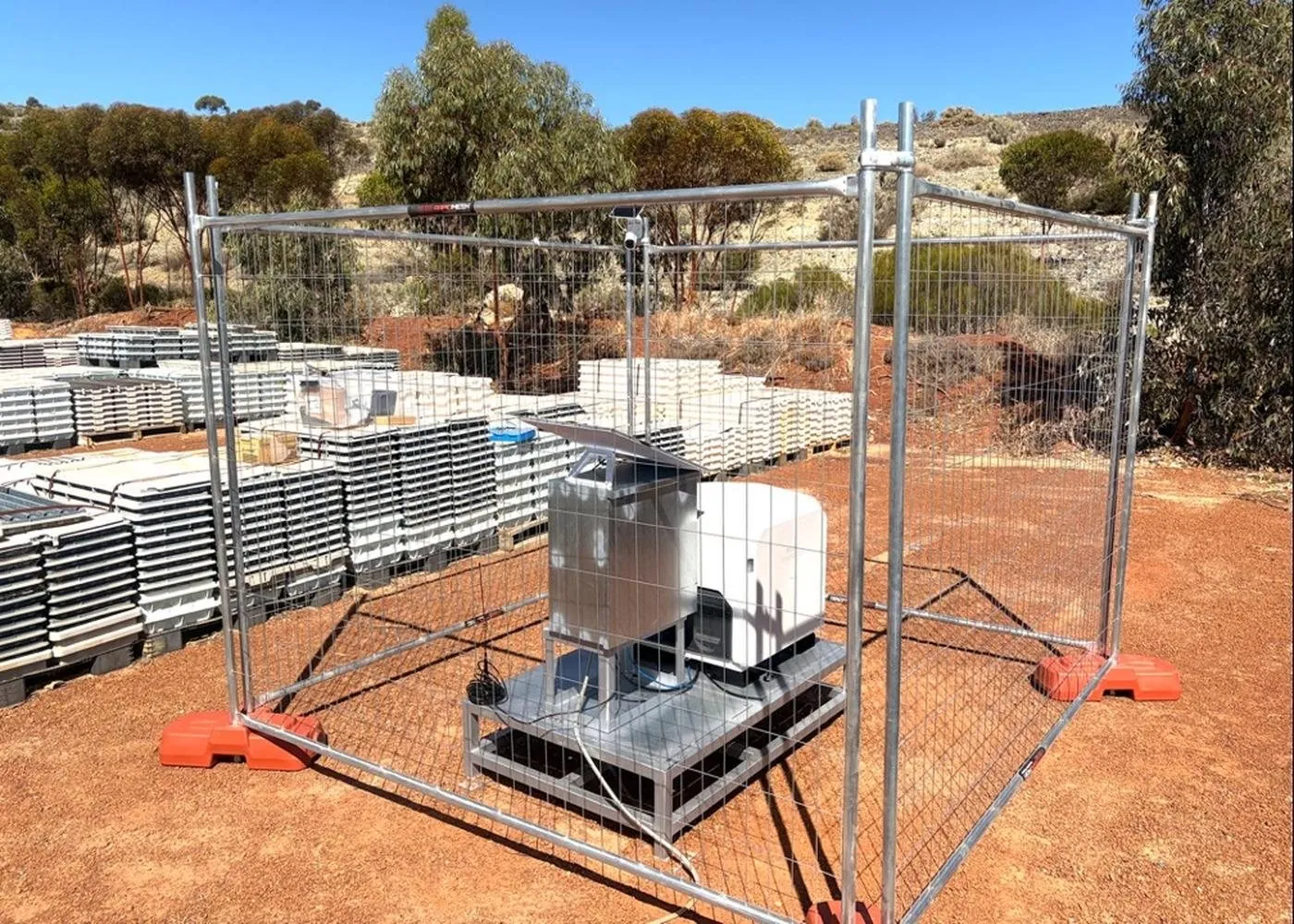 A drone dock inside a temporary safety fence on red earth at an operating gold mine